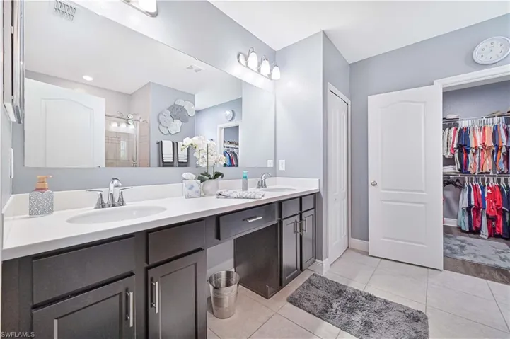 Bathroom featuring a walk in closet, double vanity, and light tile patterned floors