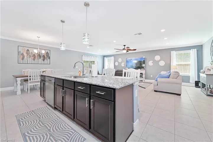 Kitchen with open floor plan, crown molding, decorative light fixtures, light stone countertops, and light tile patterned floors