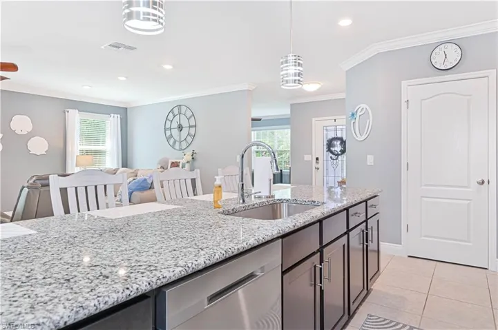 Kitchen featuring light stone countertops, crown molding, stainless steel dishwasher, recessed lighting, and healthy amount of natural light