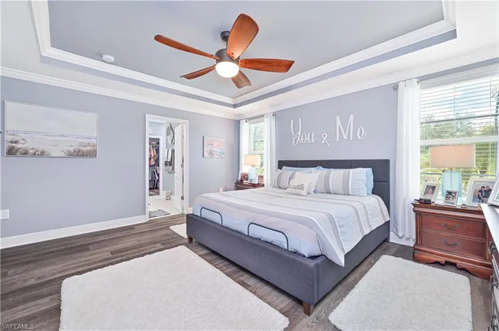 Bedroom featuring a raised ceiling, crown molding, wood finished floors, ceiling fan, and a walk in closet