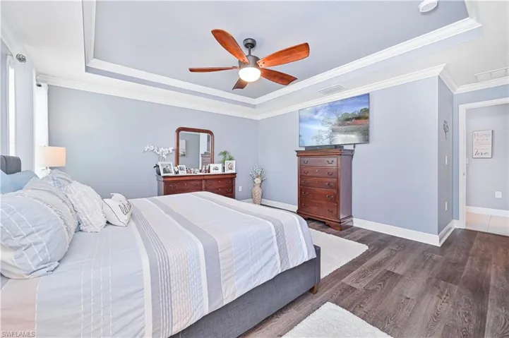 Bedroom featuring a tray ceiling, wood finished floors, ornamental molding, and ceiling fan