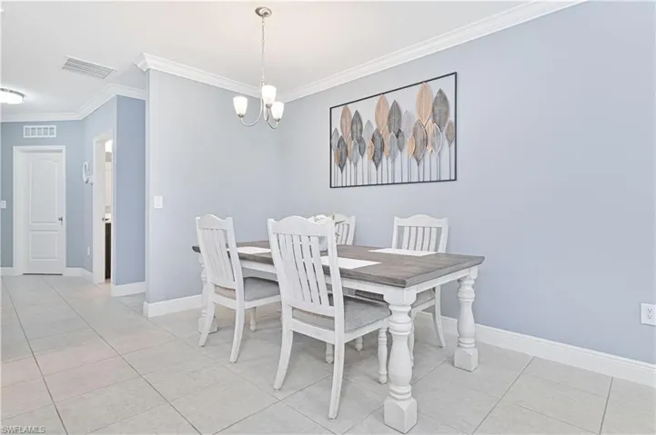 Dining space with ornamental molding, light tile patterned floors, and a chandelier