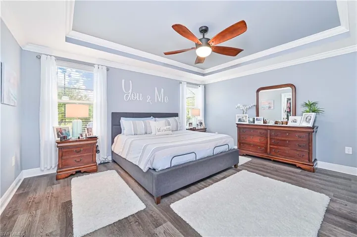 Bedroom with a tray ceiling, ornamental molding, multiple windows, dark wood-type flooring, and ceiling fan