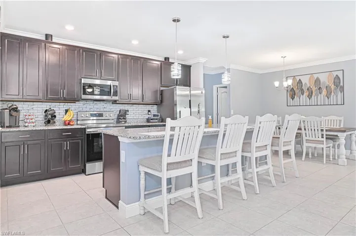 Kitchen featuring dark brown cabinets, light stone counters, stainless steel appliances, tasteful backsplash, and light tile patterned flooring