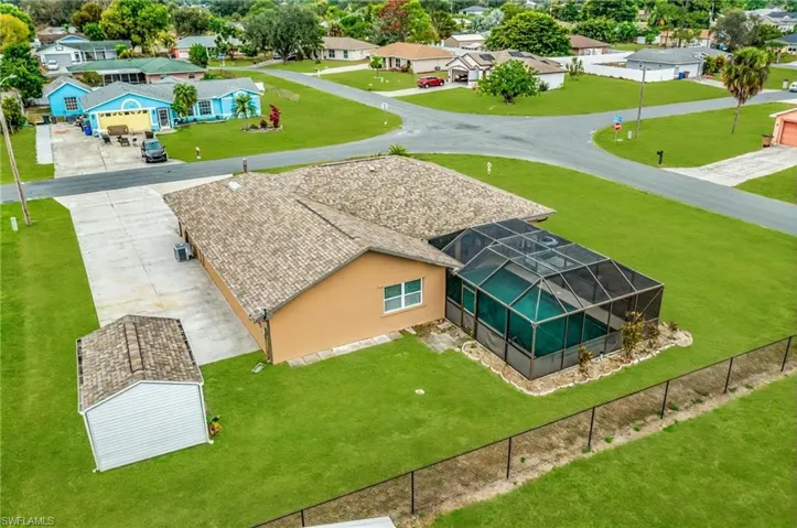 Spacious property featuring a screened-in swimming pool, a concrete driveway, a separate storage shed, lush green lawn, and a perimeter fence - Virtually Edited Image
