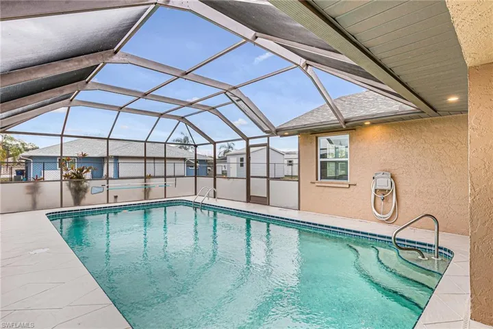 Screened enclosure featuring a rectangular pool with integrated steps, metal handrails, and a perimeter of white tile decking - Virtually Edited Image