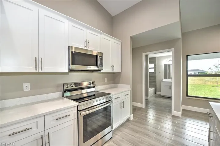 Kitchen featuring light hardwood / wood-style floors, light stone countertops, white cabinets, and stainless steel appliances