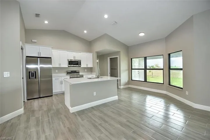 Kitchen featuring white cabinetry, sink, appliances with stainless steel finishes, lofted ceiling, and a kitchen island with sink