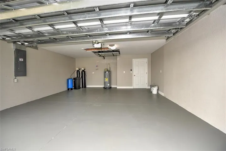 Garage with electric water heater, electric panel, and a garage door opener