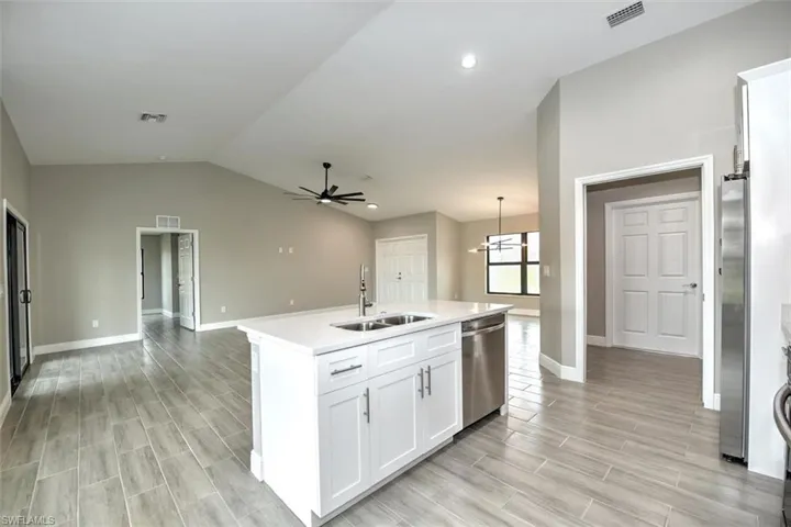 Kitchen with ceiling fan with notable chandelier, sink, vaulted ceiling, a center island with sink, and appliances with stainless steel finishes