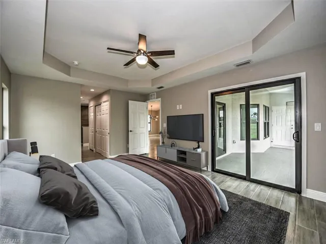 Bedroom with ceiling fan, access to outside, a tray ceiling, and wood-type flooring