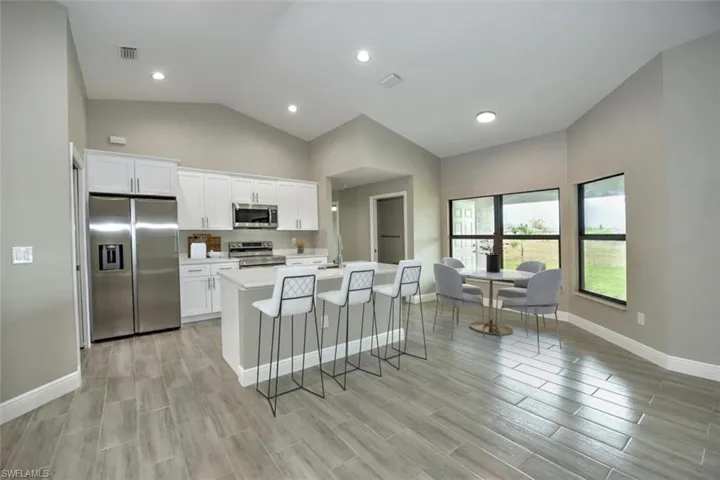 Kitchen with white cabinetry, stainless steel appliances, a breakfast bar area, vaulted ceiling, and a kitchen island with sink