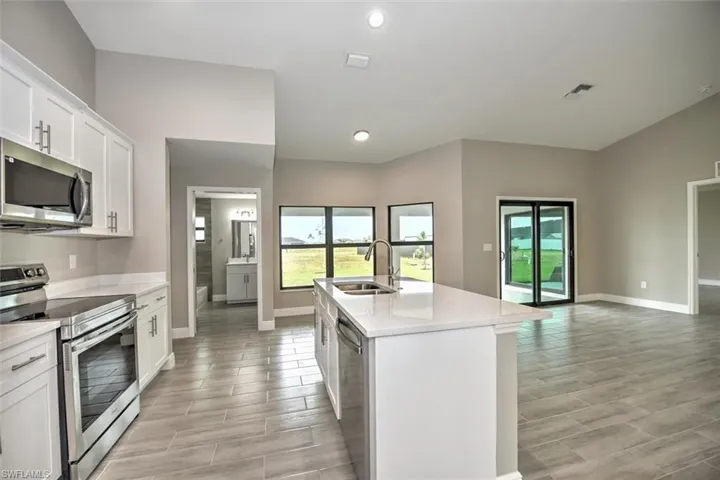 Kitchen with light tile patterned flooring, white cabinets, a kitchen island with sink, stainless steel appliances, and sink