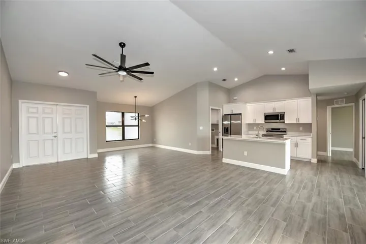 Unfurnished living room with high vaulted ceiling, light hardwood / wood-style flooring, sink, and ceiling fan