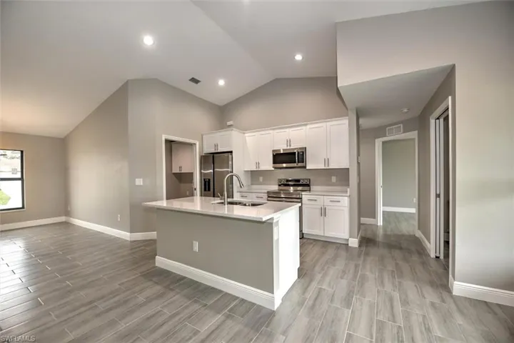 Kitchen featuring sink, appliances with stainless steel finishes, white cabinets, and an island with sink