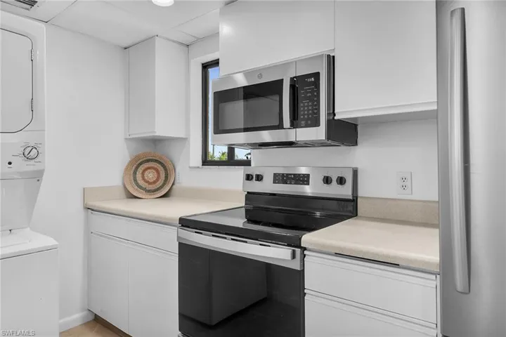 Kitchen with stainless steel appliances, white cabinets, light countertops, and stacked washer and clothes dryer
