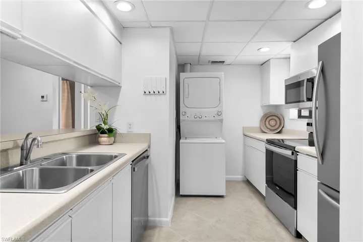 Kitchen featuring appliances with stainless steel finishes, white cabinets, light countertops, stacked washer / dryer, and a drop ceiling
