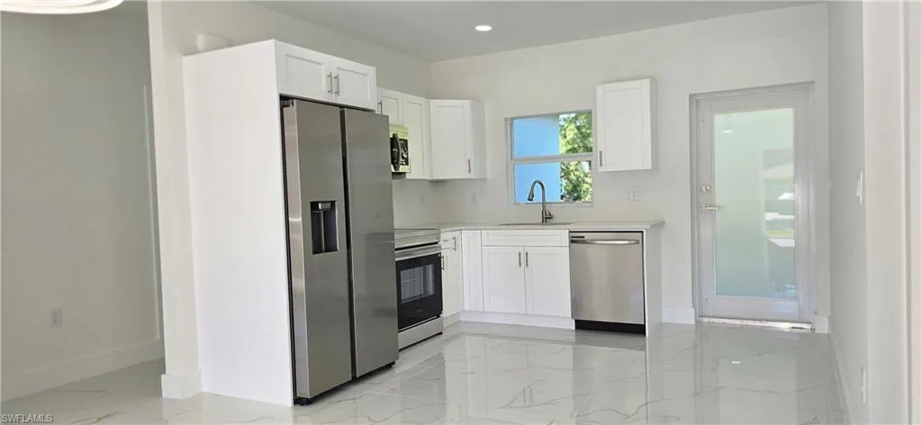 Kitchen featuring white cabinetry, stainless steel appliances, light marble finish floors, recessed lighting, and light stone counters