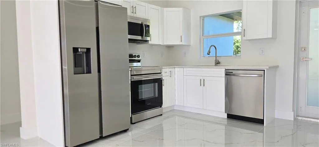 Kitchen featuring stainless steel appliances, white cabinets, light marble finish flooring, and light stone countertops