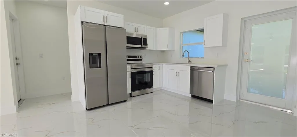 Kitchen featuring stainless steel appliances, white cabinets, light marble finish flooring, and recessed lighting