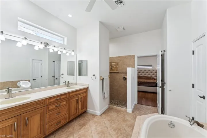 Bathroom with tile patterned flooring, vanity, ceiling fan, and a tub to relax in