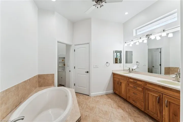 Bathroom with vanity, tiled tub, tile patterned floors, and ceiling fan