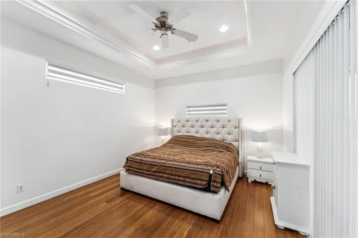 Bedroom with dark hardwood / wood-style floors, a raised ceiling, and ceiling fan