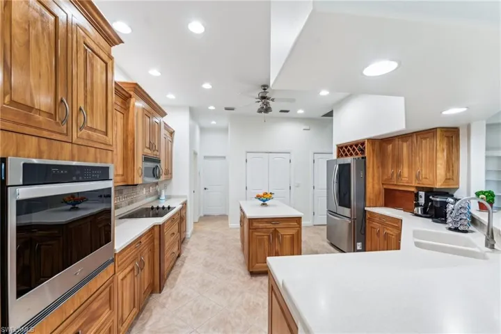 Kitchen with sink, light tile patterned floors, appliances with stainless steel finishes, a kitchen island, and decorative backsplash