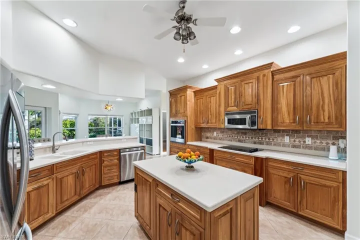 Kitchen featuring sink, light tile patterned floors, appliances with stainless steel finishes, a center island, and decorative backsplash