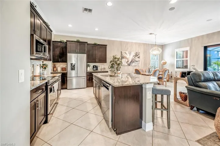 Kitchen featuring light tile patterned floors, light stone countertops, stainless steel appliances, a kitchen bar, and a kitchen island with sink