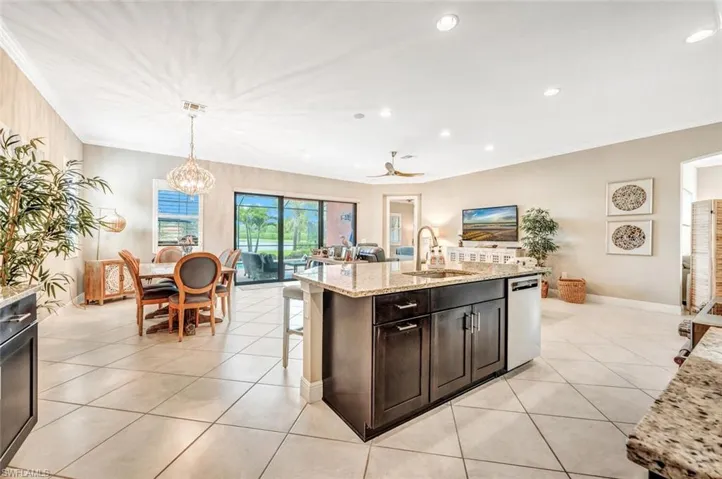 Kitchen featuring ceiling fan with notable chandelier, light stone counters, a breakfast bar area, a kitchen island with sink, and stainless steel dishwasher