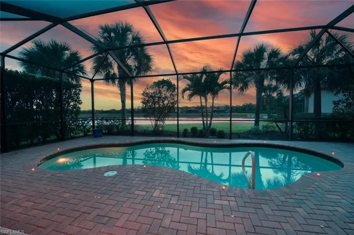 Pool at dusk featuring glass enclosure, an outdoor pool, a patio area, and a water view