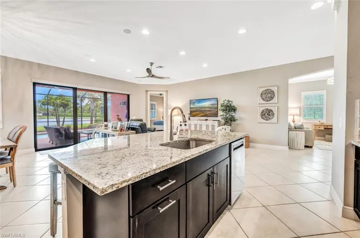 Kitchen with light stone counters, an island with sink, sink, ceiling fan, and light tile patterned flooring