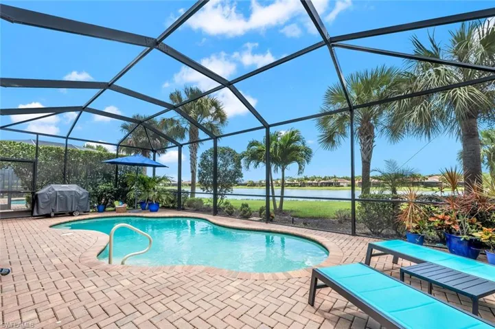 View of pool featuring grilling area, glass enclosure, a water view, and a patio