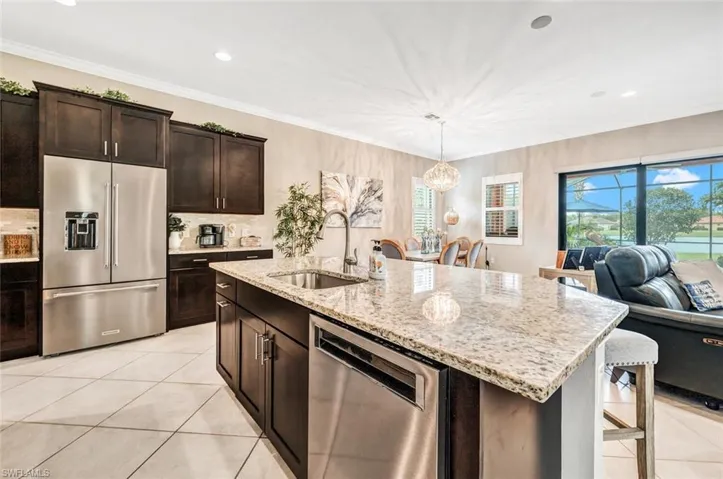 Kitchen featuring decorative light fixtures, light stone countertops, appliances with stainless steel finishes, a kitchen island with sink, and sink