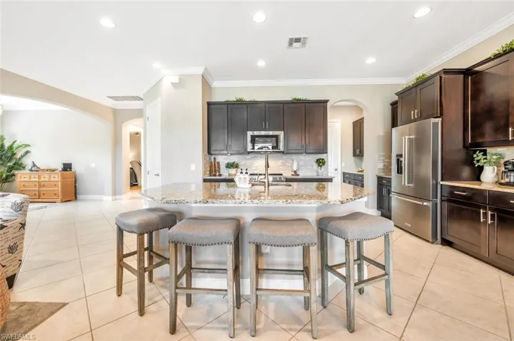 Kitchen with light tile patterned floors, appliances with stainless steel finishes, light stone countertops, a breakfast bar area, and a center island with sink