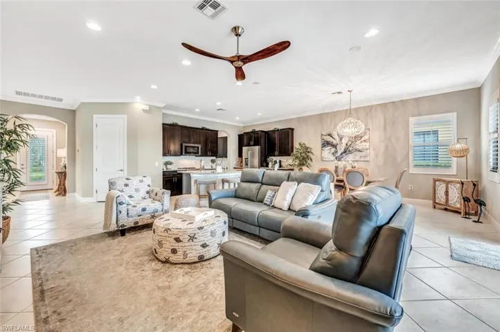 Tiled living room featuring ceiling fan with notable chandelier, plenty of natural light, and crown molding