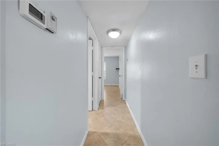 Hallway featuring light blue walls, tan tile flooring, white trim, and a contemporary ceiling light fixture