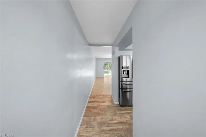 Hallway with tile flooring and a stainless steel refrigerator visible through an arched entryway