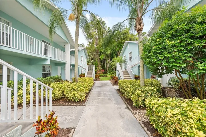 Landscaped pathway between two-story residential buildings featuring white railings and mature palm trees