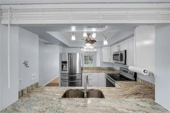Kitchen featuring a double stainless steel sink, stone countertops with a matching backsplash, white cabinetry with stainless steel hardware, and a suite of stainless steel appliances