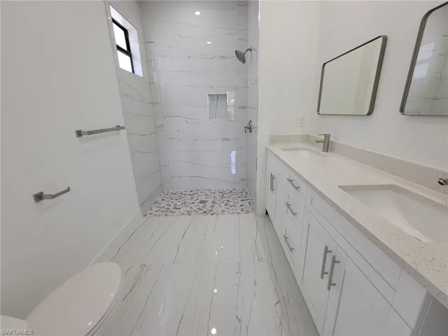 Bathroom with tile patterned floors, dual vanity, toilet, and a tile shower