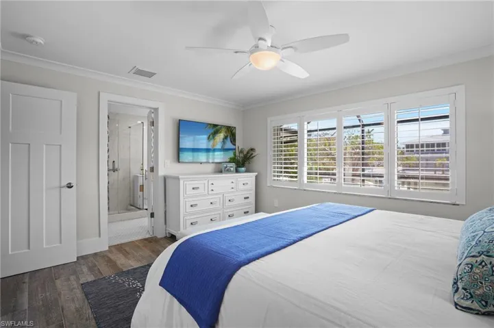 Bedroom with ceiling fan, connected bathroom, wood finished floors, visible vents, and crown molding. Virtually Edited Image