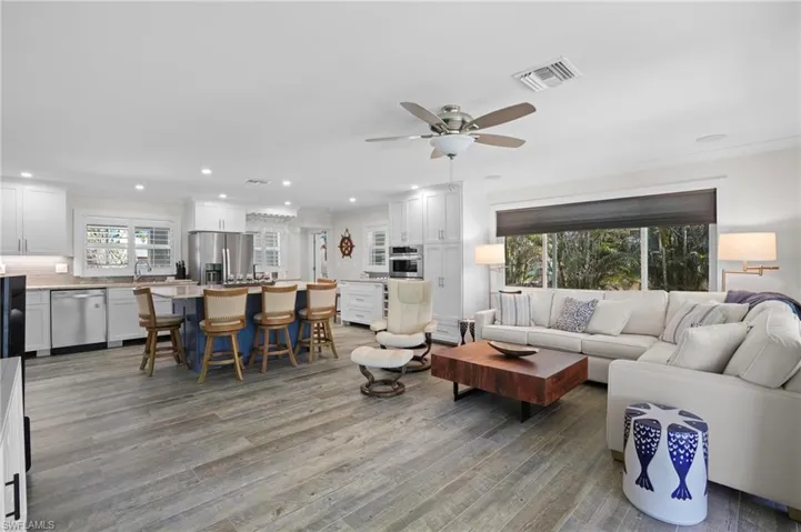 Living area with light wood-style flooring, a ceiling fan, visible vents, and recessed lighting. Virtually Edited Image