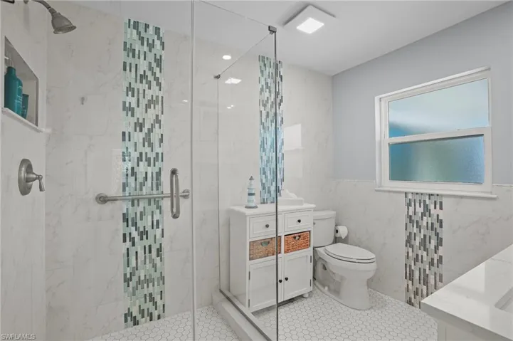 Full bath featuring tile patterned flooring, toilet, vanity, tile walls, and a shower stall. Virtually Edited Image