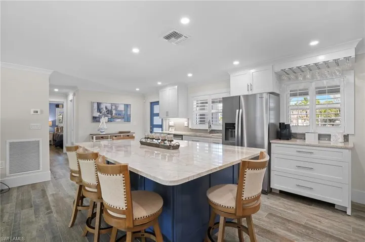 Kitchen with crown molding, wood finished floors, visible vents, and white cabinets. Virtually Edited Image