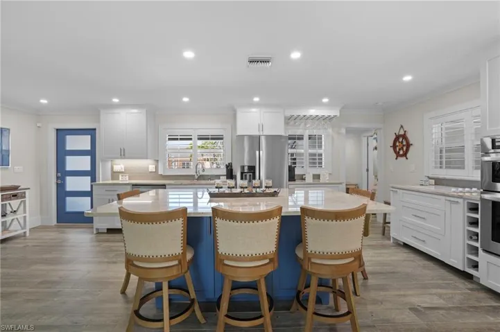 Kitchen with visible vents, dark wood-style floors, a kitchen island, appliances with stainless steel finishes, and ornamental molding. Virtually Edited Image