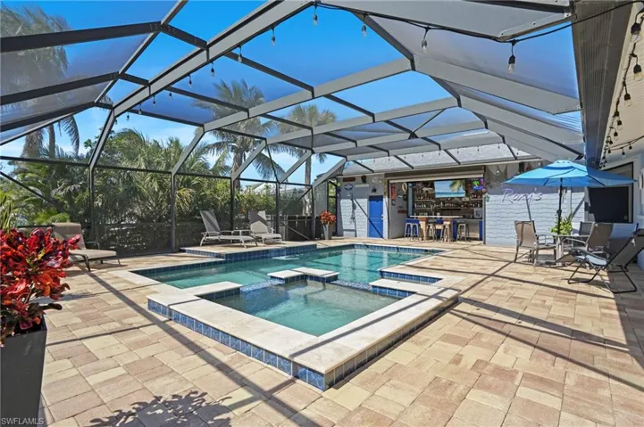 View of swimming pool with outdoor dry bar, glass enclosure, a patio area, and a pool with connected hot tub. Virtually Edited Image