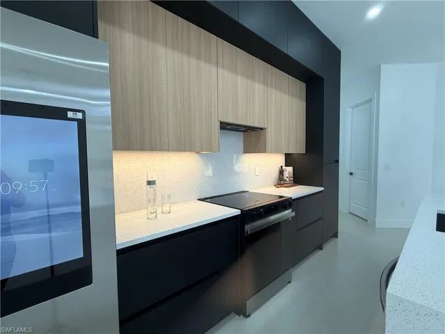 Kitchen featuring modern cabinets, stainless steel fridge, electric range, light stone counters, and concrete floors