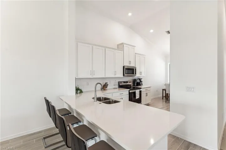 Kitchen featuring white cabinets, tasteful backsplash, stainless steel appliances, a peninsula, and wood tiled floors